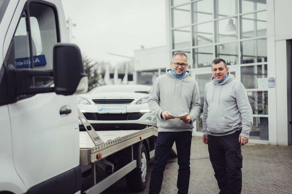 Mathias Warsinksi kauft ein Auto von einem glücklichen Kunden. Das Auto wird im Hintergund auf einen Transporter geladen.