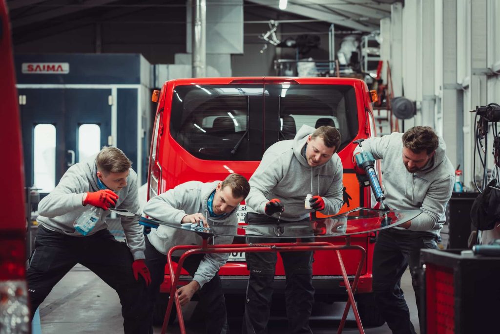 Vier Mechaniker bereiten eine Winschutzscheibe für den Einbau vor.